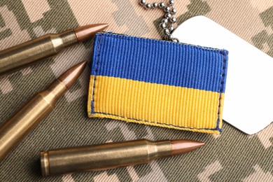 Photo of Ukrainian army patch, bullets and ID tags on pixel military camouflage, flat lay
