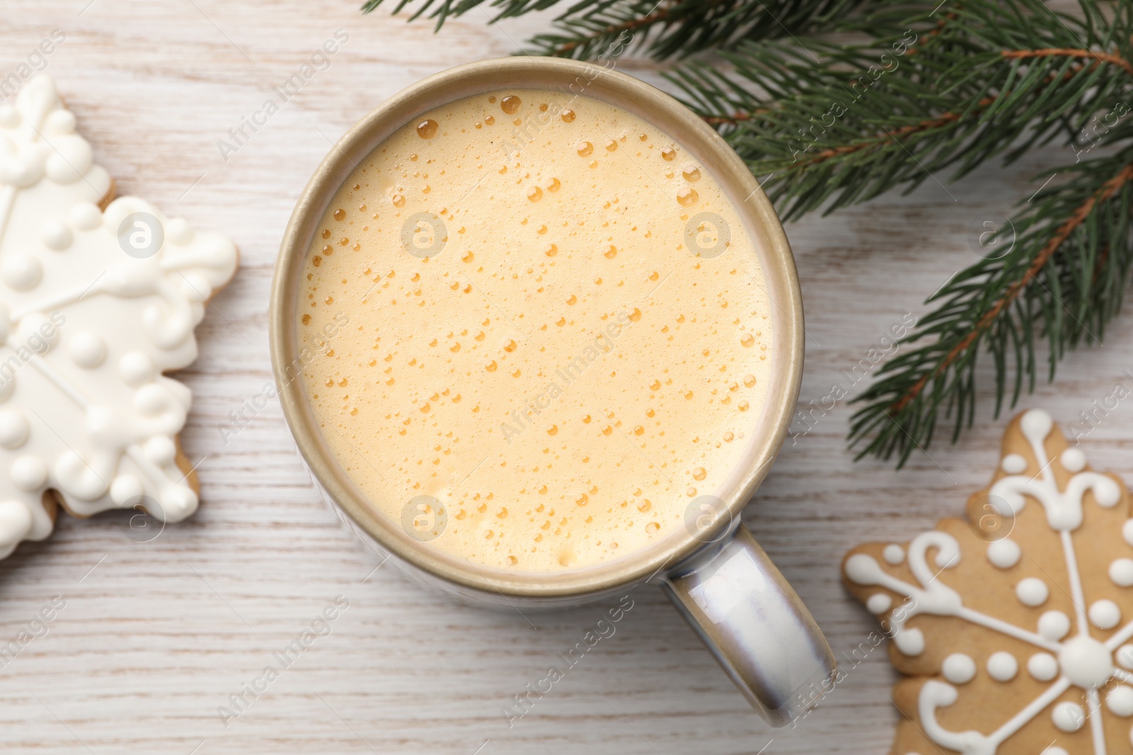 Photo of Cup of delicious eggnog, fir branch and cookies on wooden table, flat lay