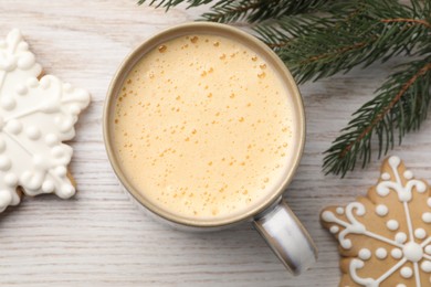 Photo of Cup of delicious eggnog, fir branch and cookies on wooden table, flat lay