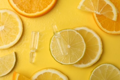 Photo of Skincare ampoules with vitamin C and citrus slices on yellow background, flat lay