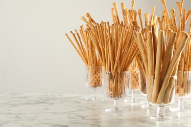Delicious grissini sticks served in glasses on white marble table. Space for text