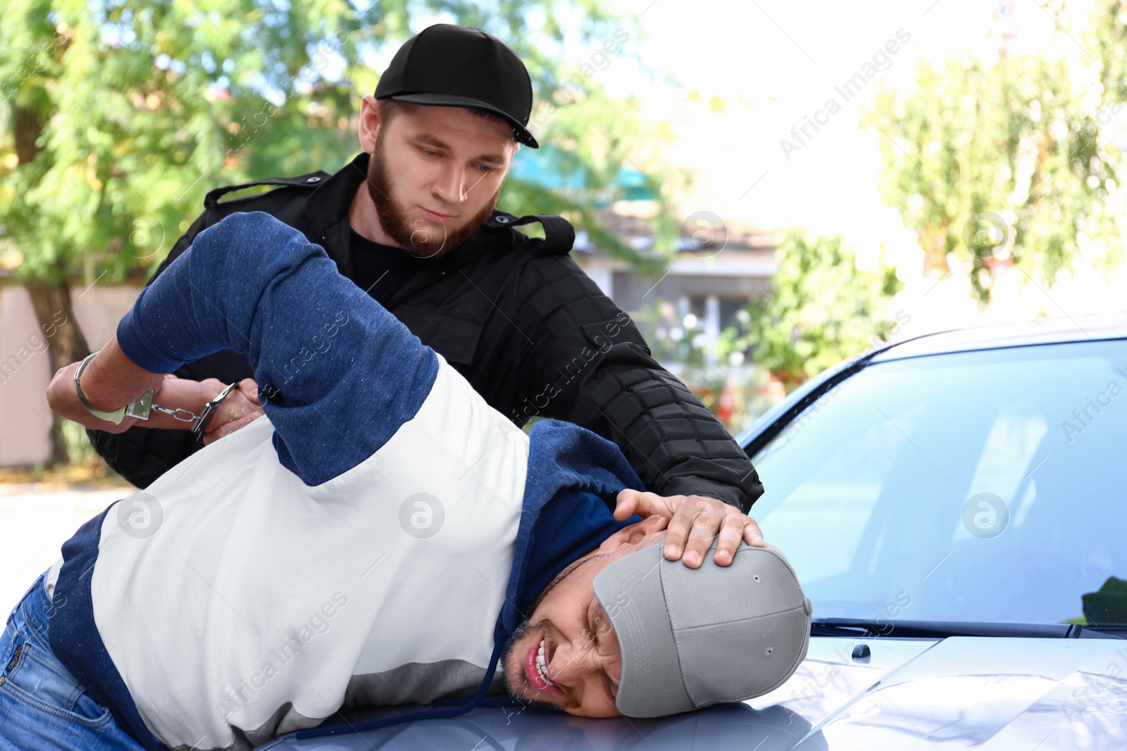 Photo of Police officer arresting criminal near car outdoors