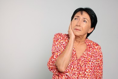 Photo of Senior woman suffering from ear pain on light grey background. Space for text