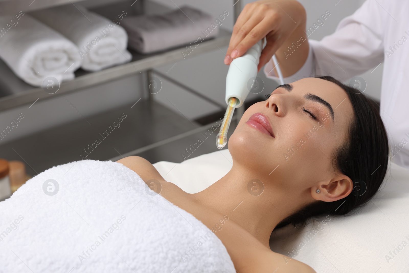 Photo of Young woman undergoing face rejuvenation procedure with darsonval in salon