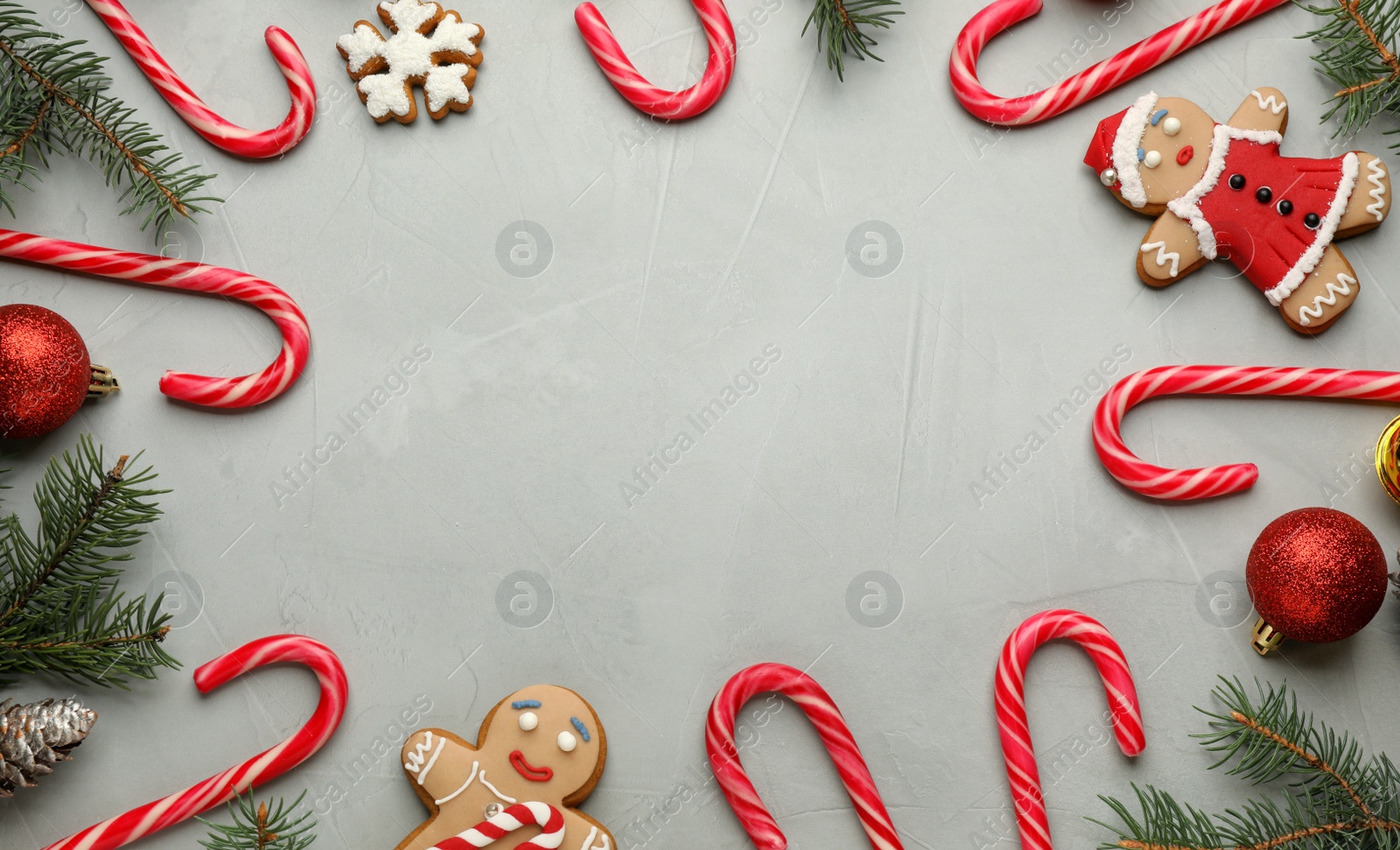 Photo of Frame of tasty candy canes and Christmas decor on grey table, flat lay. Space for text