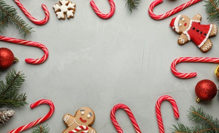 Photo of Frame of tasty candy canes and Christmas decor on grey table, flat lay. Space for text