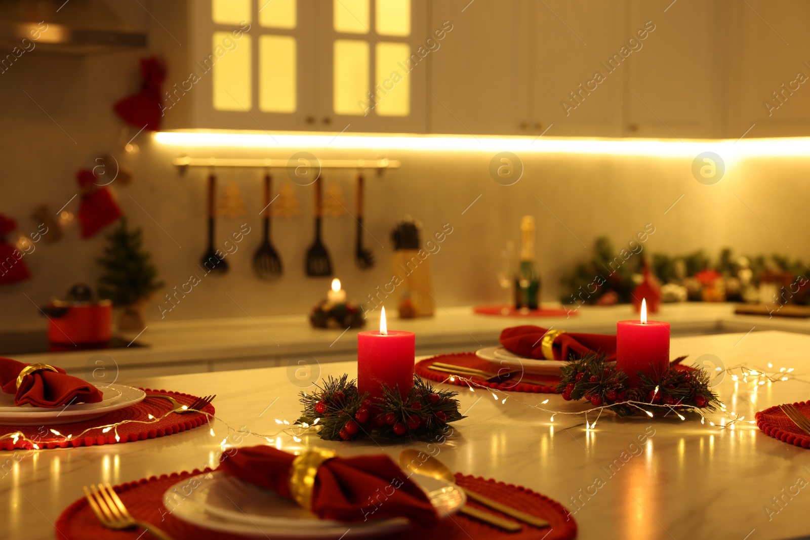 Photo of Christmas table setting with burning candles and festive decor in kitchen