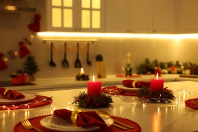 Photo of Christmas table setting with burning candles and festive decor in kitchen