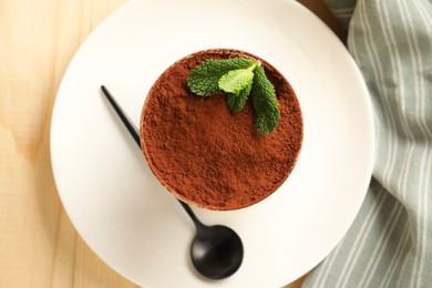 Photo of Tasty tiramisu and mint in glass on light wooden table, top view