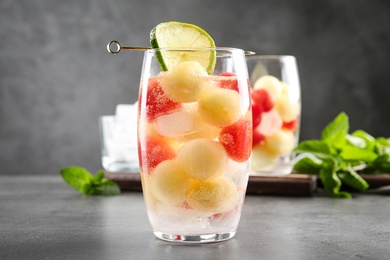 Photo of Glass of melon and watermelon ball cocktail on grey table