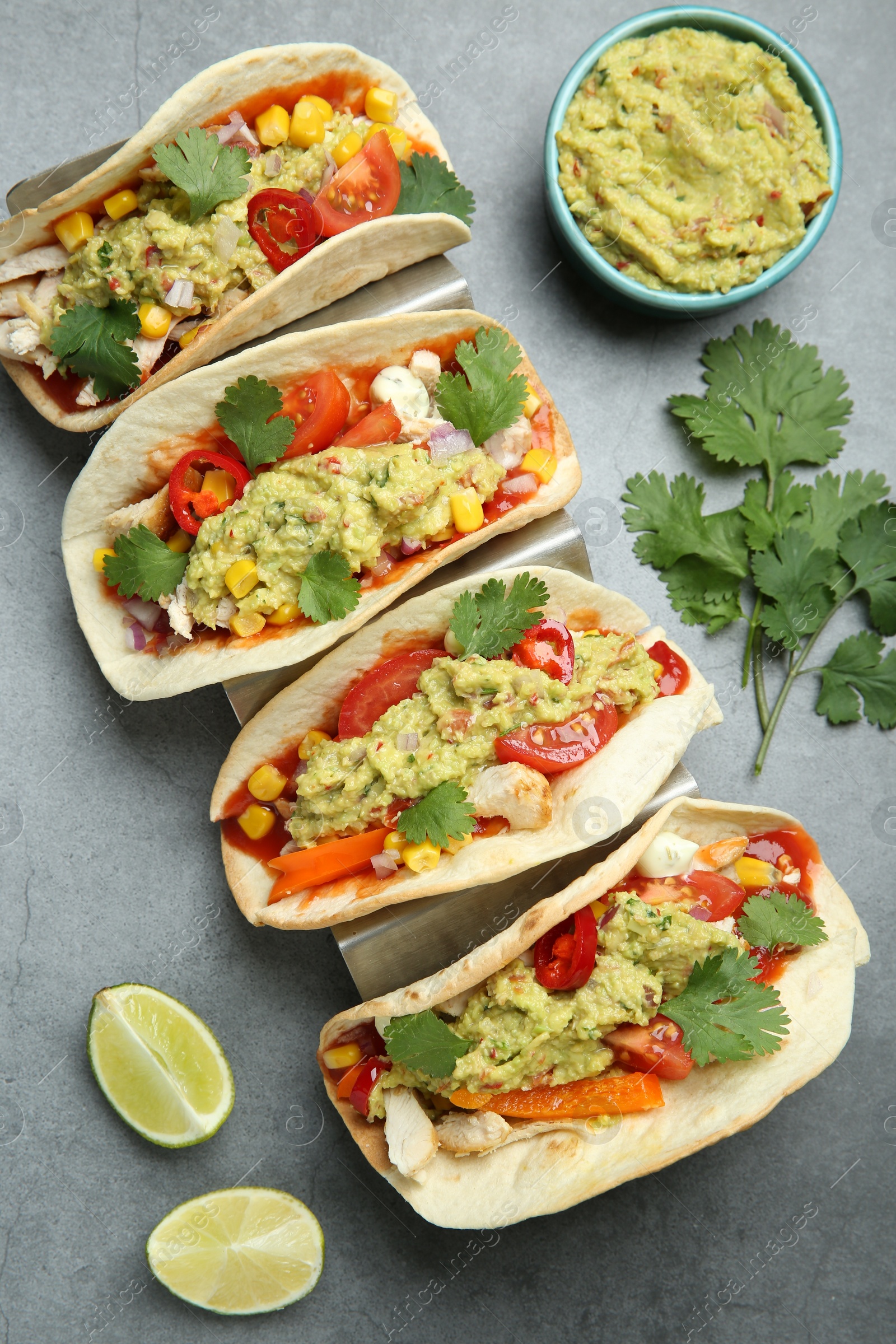 Photo of Delicious tacos with guacamole, meat and vegetables served on grey table, flat lay