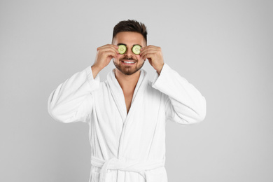 Photo of Young man in bathrobe with cucumber slices on light grey background