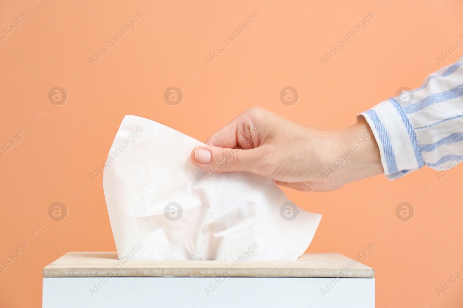 Photo of Woman taking paper tissue from holder on light brown background, closeup