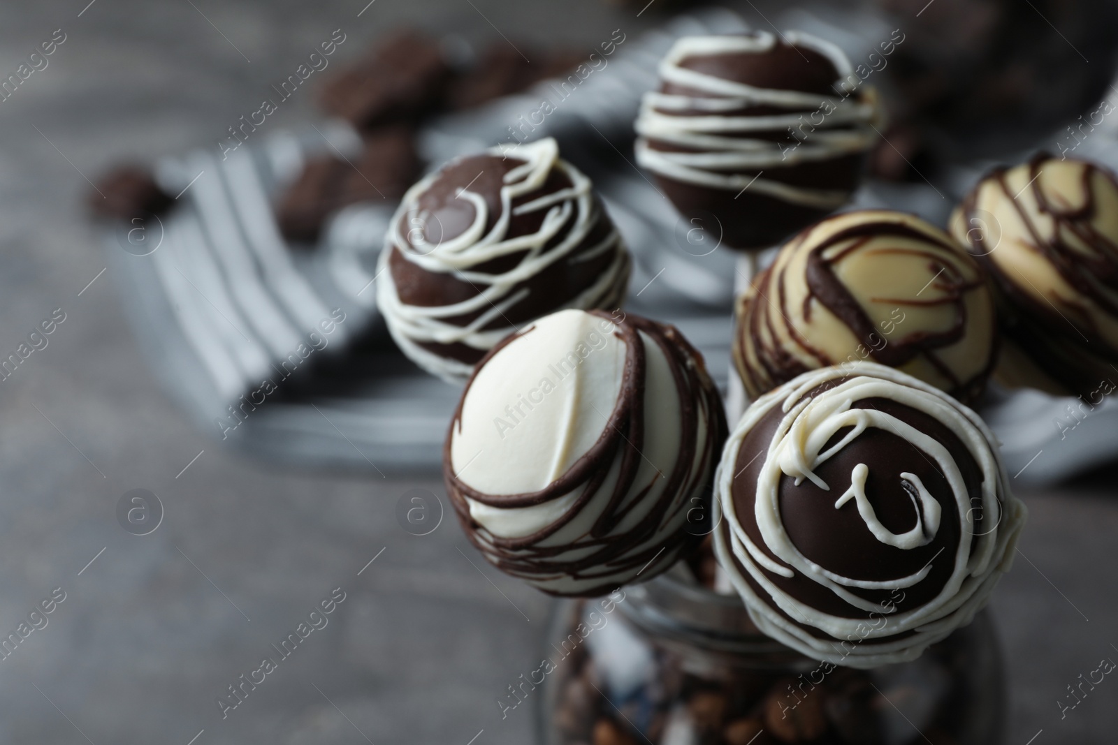 Photo of Yummy cake pops coated with chocolate in glass jar on table, closeup. Space for text