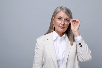 Photo of Portrait of beautiful senior woman in glasses on grey background. Space for text