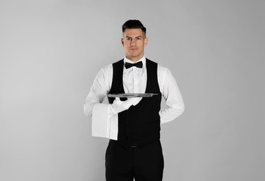 Photo of Handsome butler with tray on light grey background