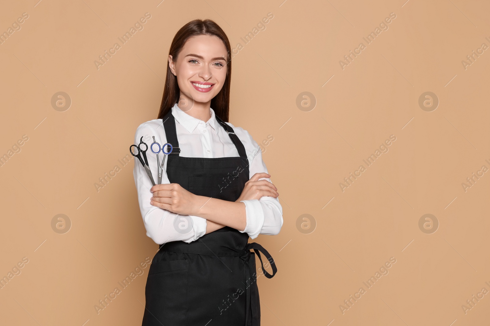 Photo of Portrait of happy hairdresser with professional scissors on beige background. Space for text
