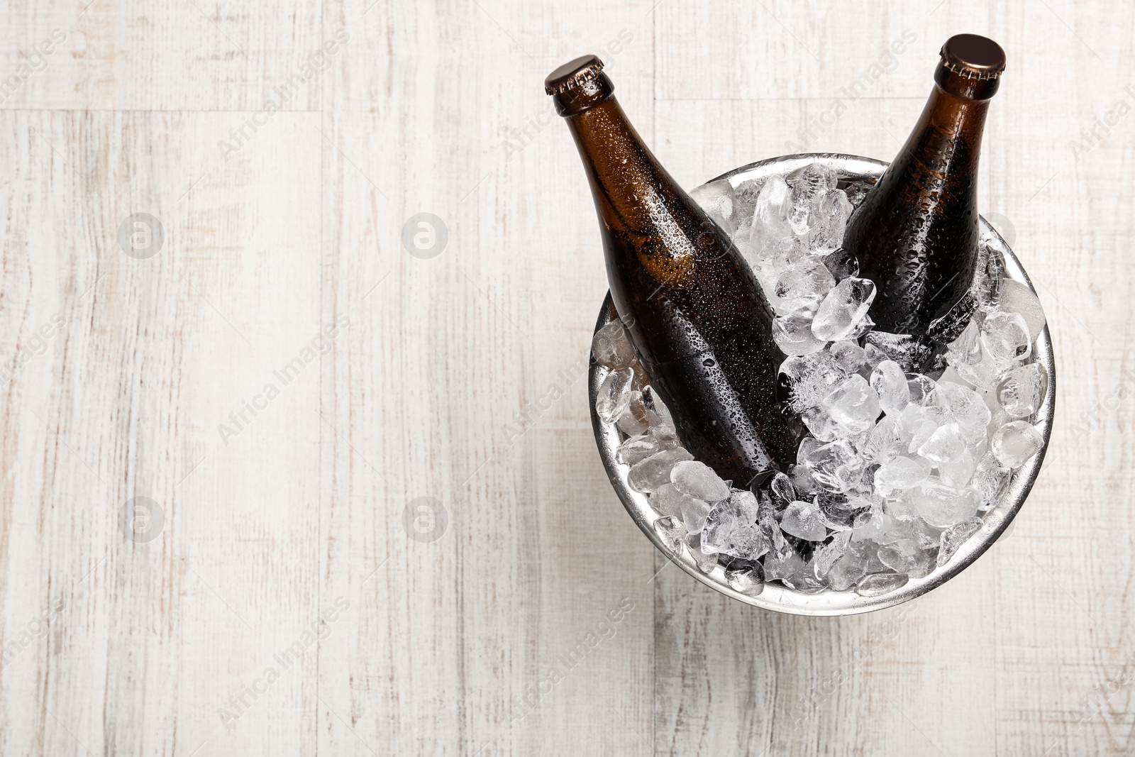 Photo of Beer in metal bucket with ice on white wooden table, top view. Space for text