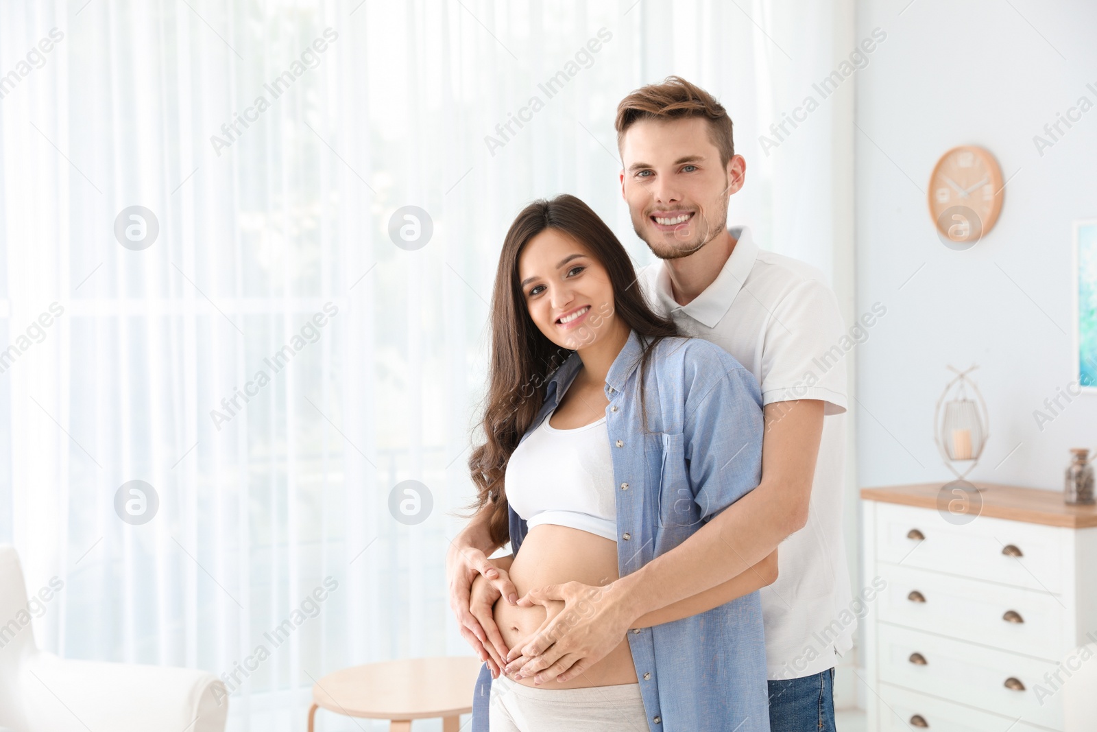Photo of Pregnant woman and her husband showing heart with hands at home. Space for text