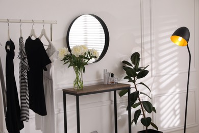 Photo of Rack with clothes near console table in room. Interior design