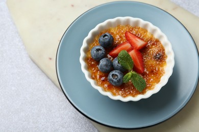 Photo of Delicious creme brulee with berries and mint in bowl on grey textured table, above view