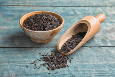 Photo of Bowl and scoop with uncooked black rice on blue wooden background