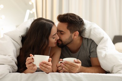 Photo of Cute young couple kissing under warm blanket in bed indoors