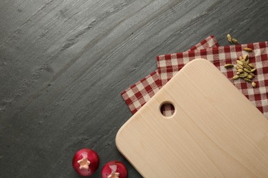 Photo of Wooden cutting board, kitchen towel and cardamom pods on dark grey table, flat lay. Space for text