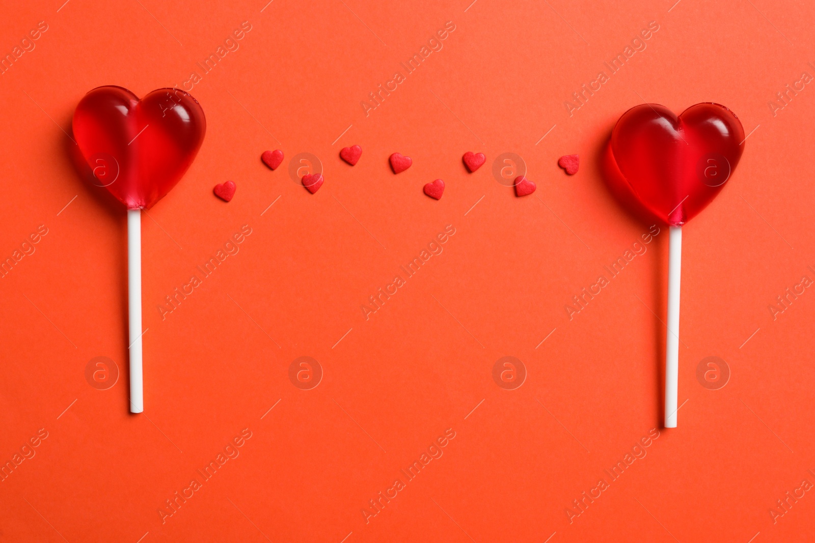 Photo of Sweet heart shaped lollipops and sprinkles on coral background, flat lay. Valentine's day celebration