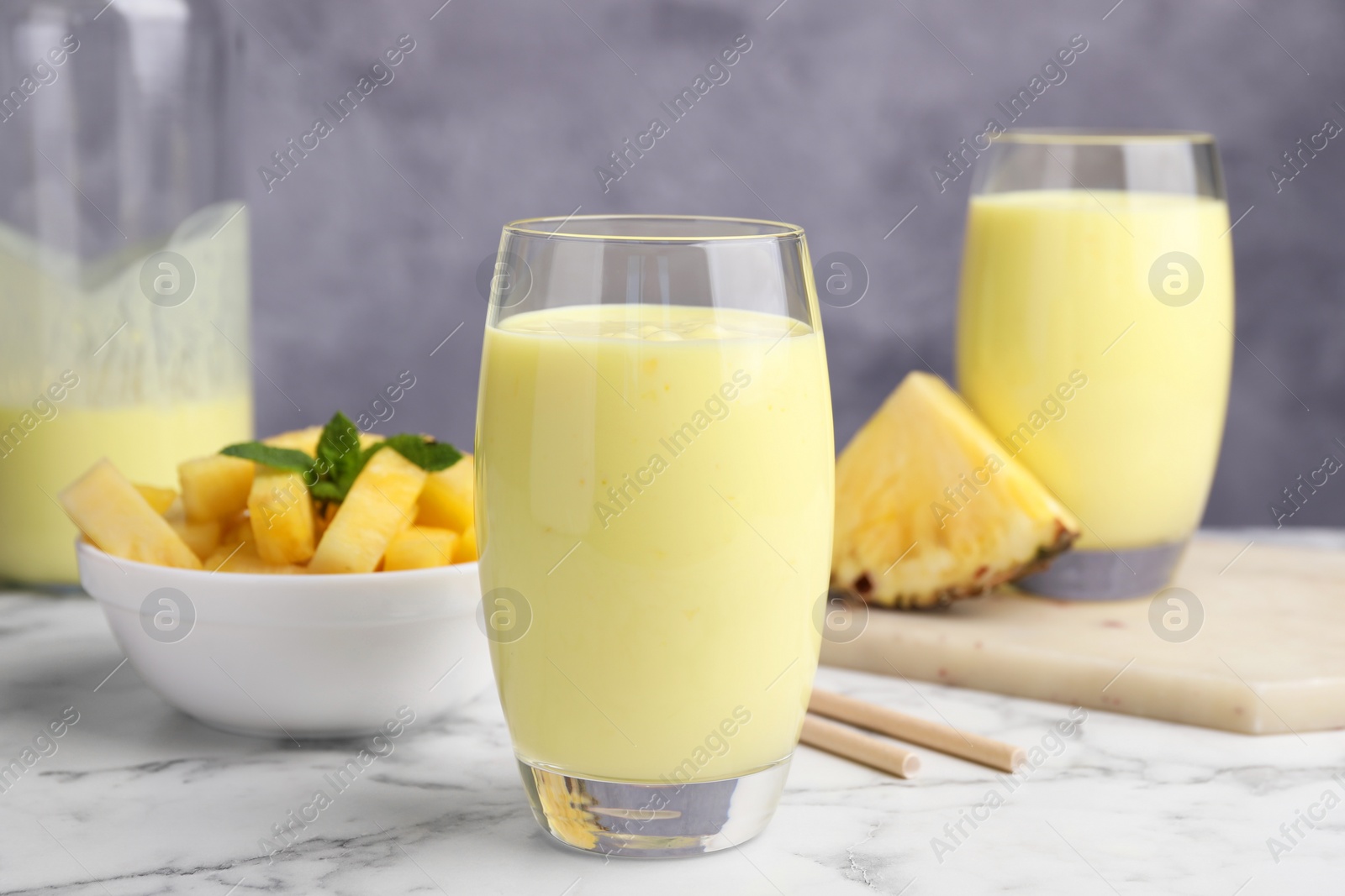 Photo of Tasty pineapple smoothie and sliced fruit on white marble table