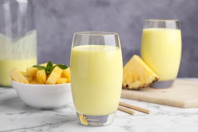 Tasty pineapple smoothie and sliced fruit on white marble table