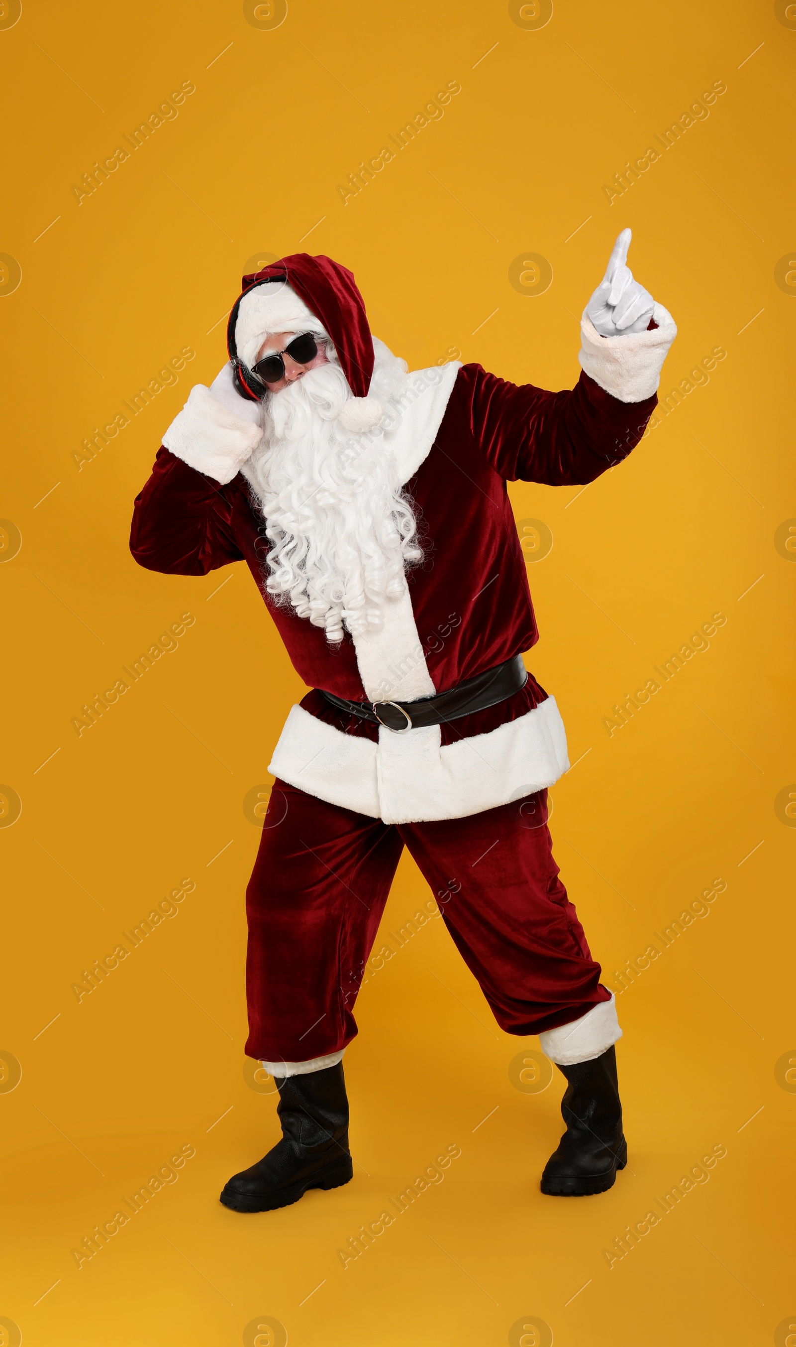 Photo of Santa Claus with headphones listening to Christmas music on yellow background