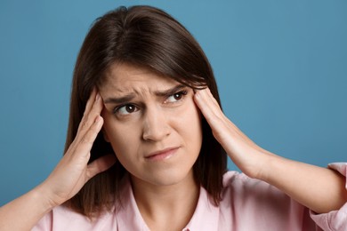 Photo of Young woman suffering from migraine on light blue background