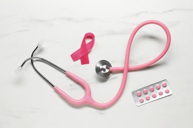 Photo of Pink ribbon, stethoscope and pills on white marble table, flat lay. Breast cancer awareness
