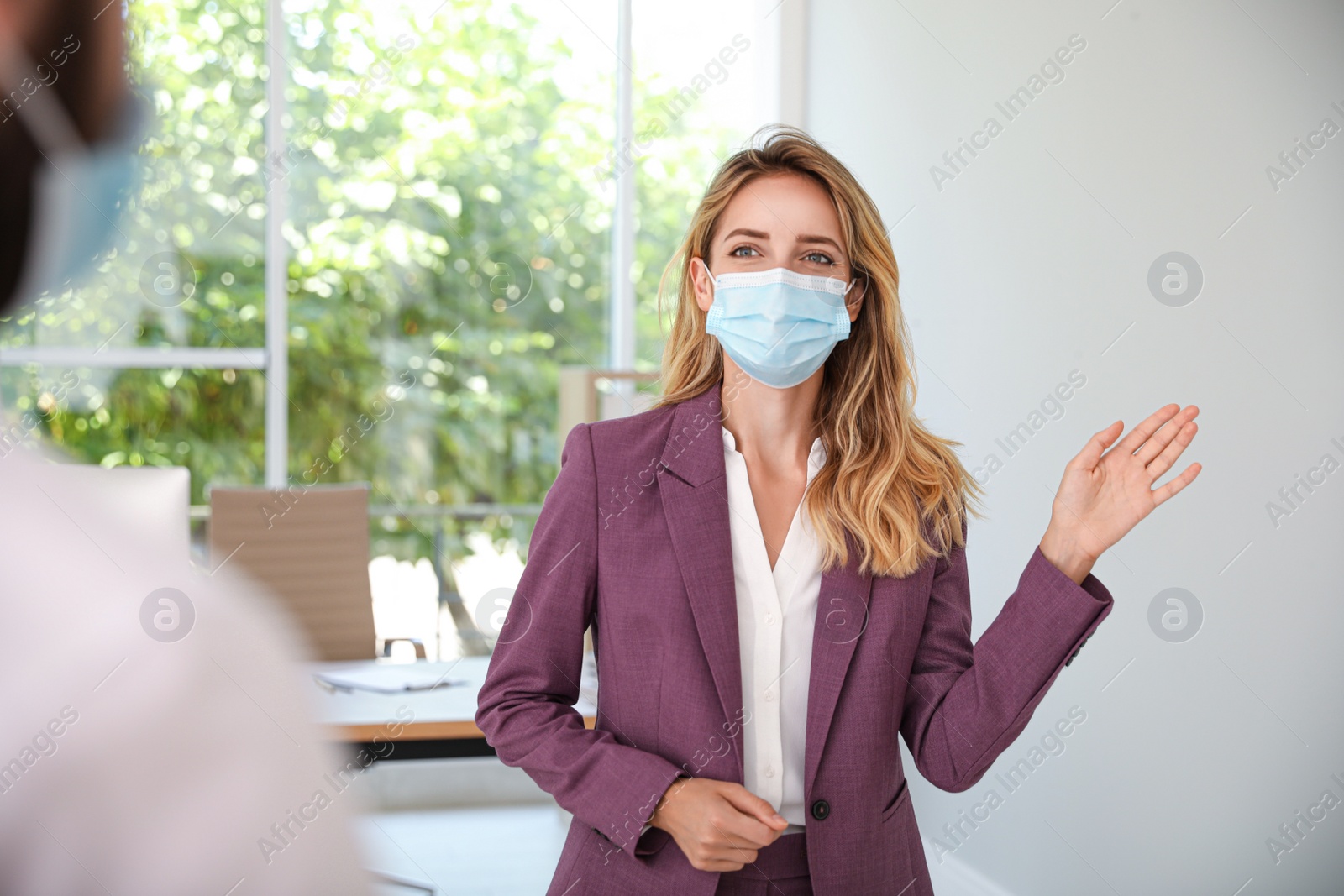 Photo of Woman in protective mask saying hello in office. Keeping social distance during coronavirus pandemic
