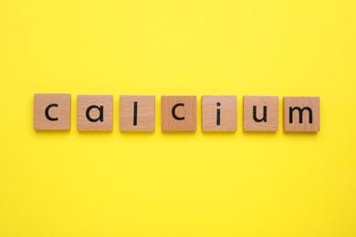 Photo of Word Calcium made of wooden cubes with letters on yellow background, top view