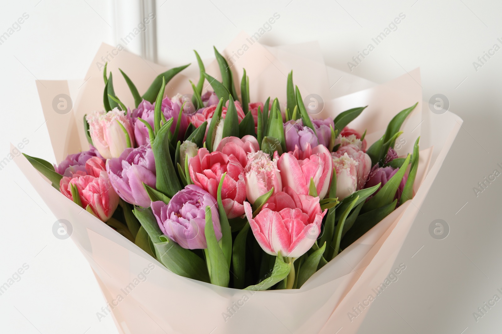 Photo of Bouquet of beautiful tulips near white wall, closeup
