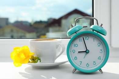 Photo of Alarm clock and cup of drink with flower on windowsill. Good morning