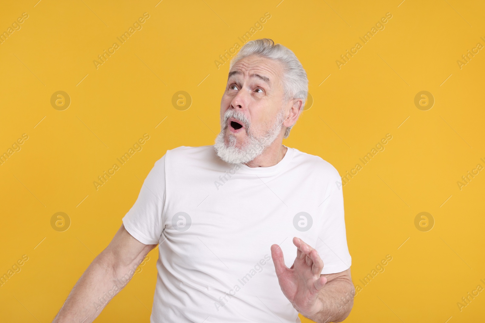 Photo of Portrait of surprised senior man on yellow background