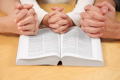 Girl and her godparents praying over Bible together at table indoors, closeup