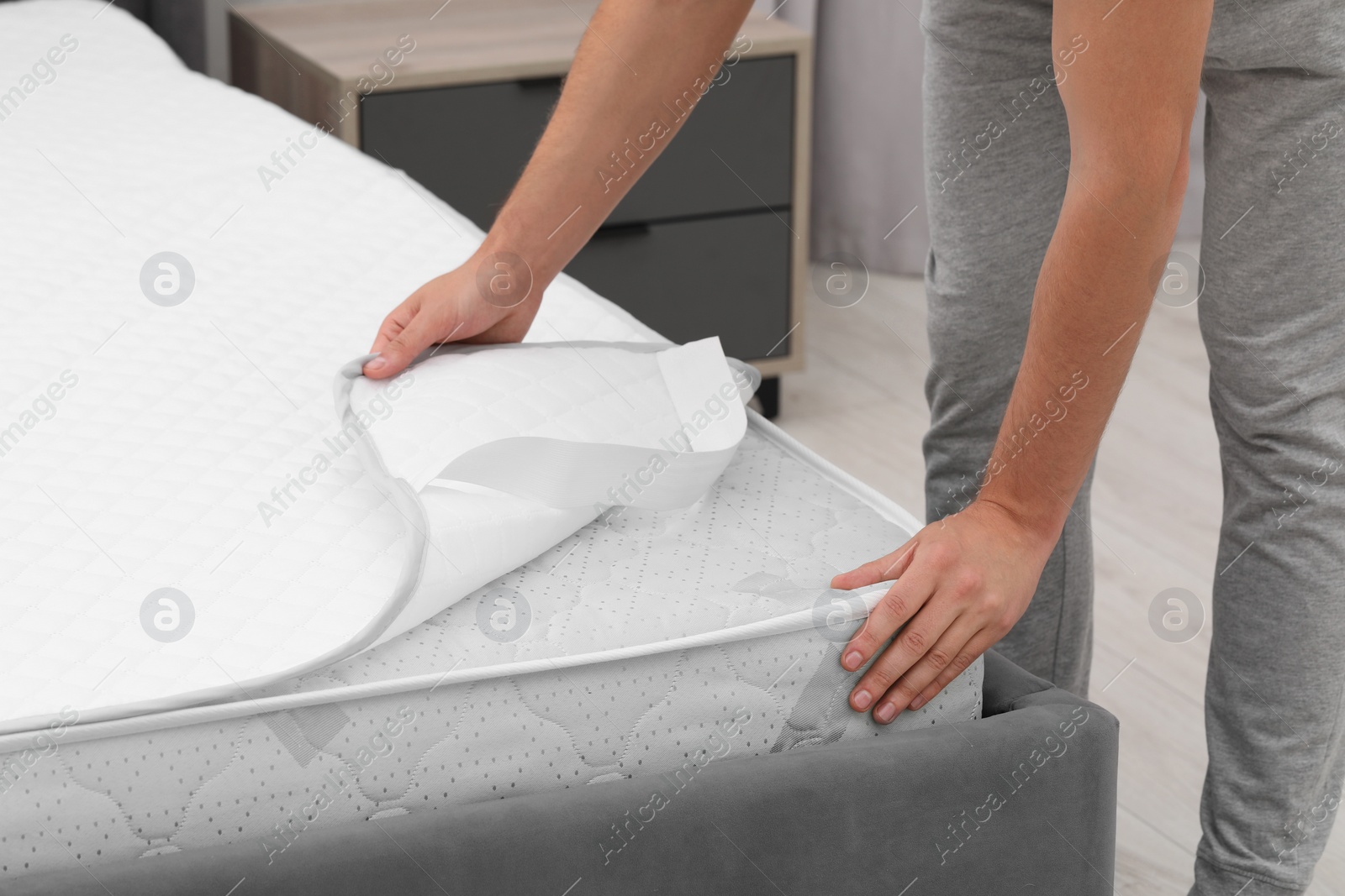 Photo of Man putting protector on mattress indoors, closeup