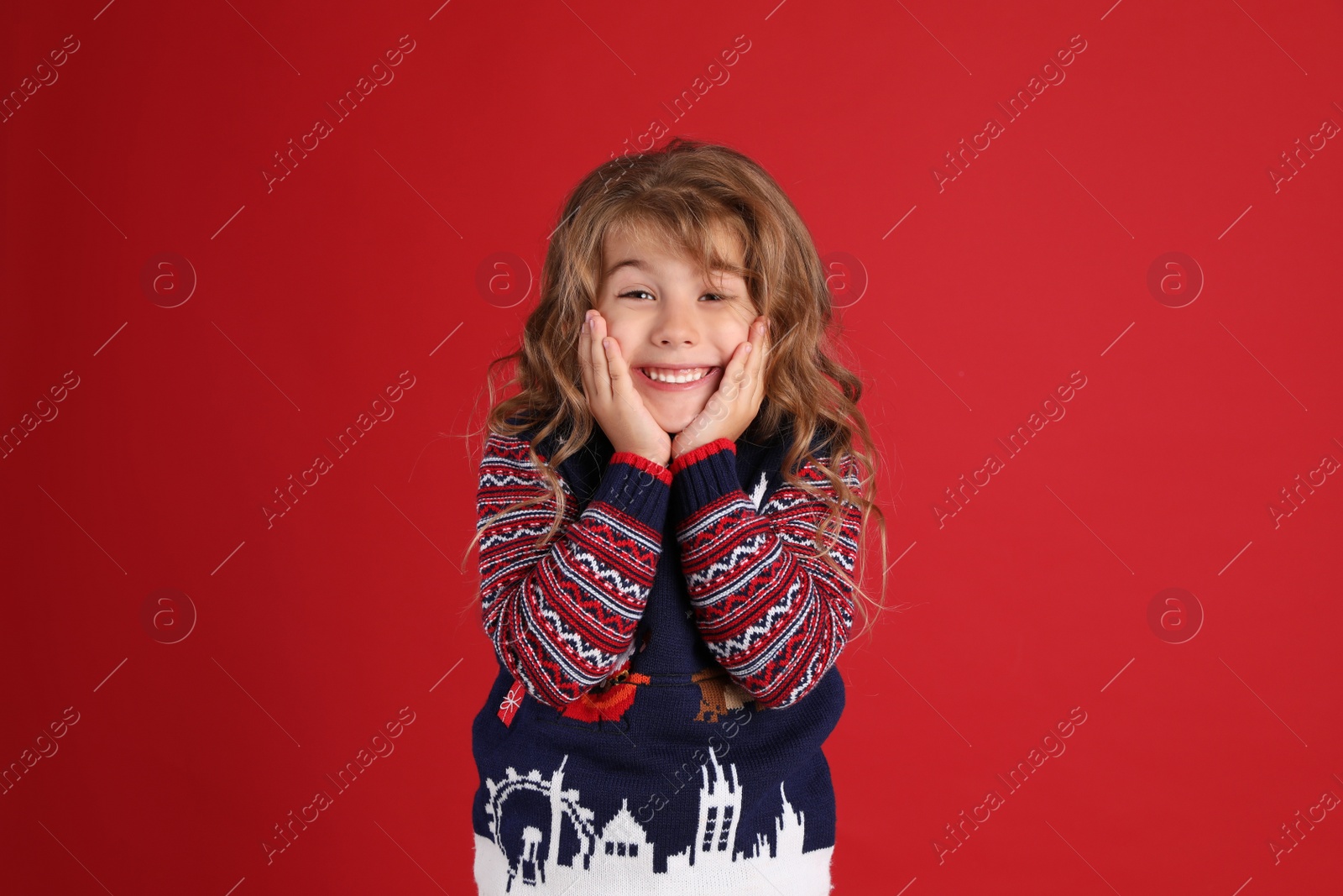 Photo of Happy little girl in Christmas sweater smiling against red background