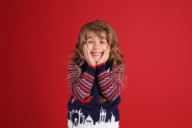 Photo of Happy little girl in Christmas sweater smiling against red background