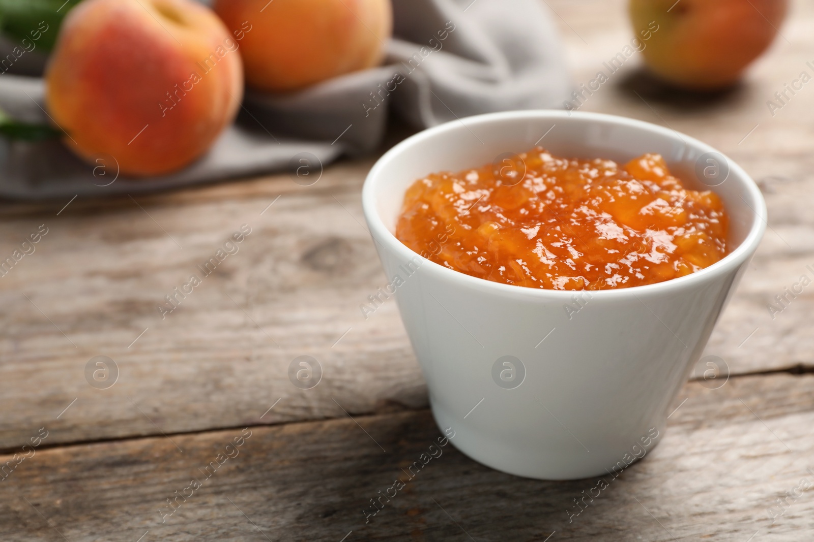 Photo of Bowl with tasty peach jam on wooden table