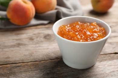 Bowl with tasty peach jam on wooden table