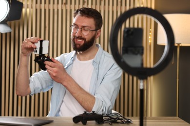 Smiling technology blogger with game controller and smartphone recording video review at home