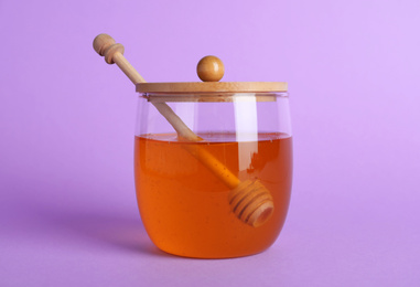 Jar of organic honey and dipper on violet background