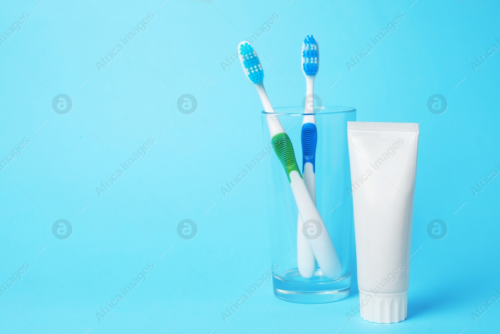 Photo of Glass with brushes and toothpaste on color background. Space for text