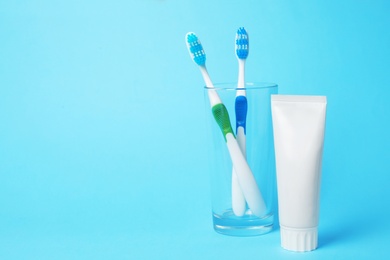 Photo of Glass with brushes and toothpaste on color background. Space for text