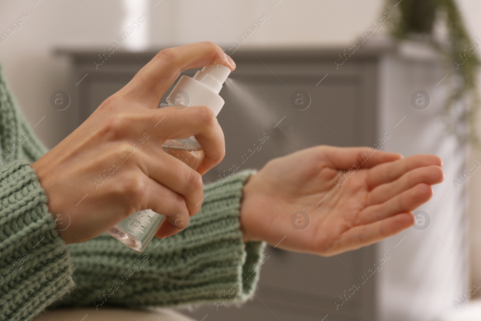 Photo of Young woman applying antiseptic spray indoors, closeup